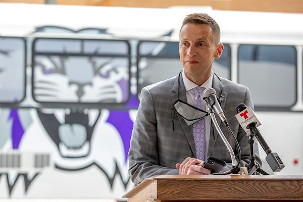 President Brad Mortensen speaking at a podium in front of a Weber State branded bus.